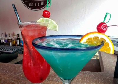 two fruity cabana bar drinks. one red and one blue. with fruit slices