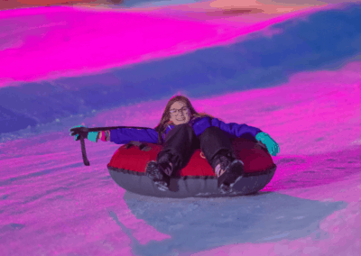kid with glasses smiling and sliding on tube at lunar lights snow tubing