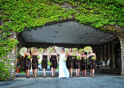 bride with bridesmaids walking under archway with green vines