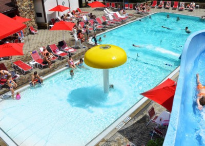 outdoor pool with slide, yellow fountain, and people having fun